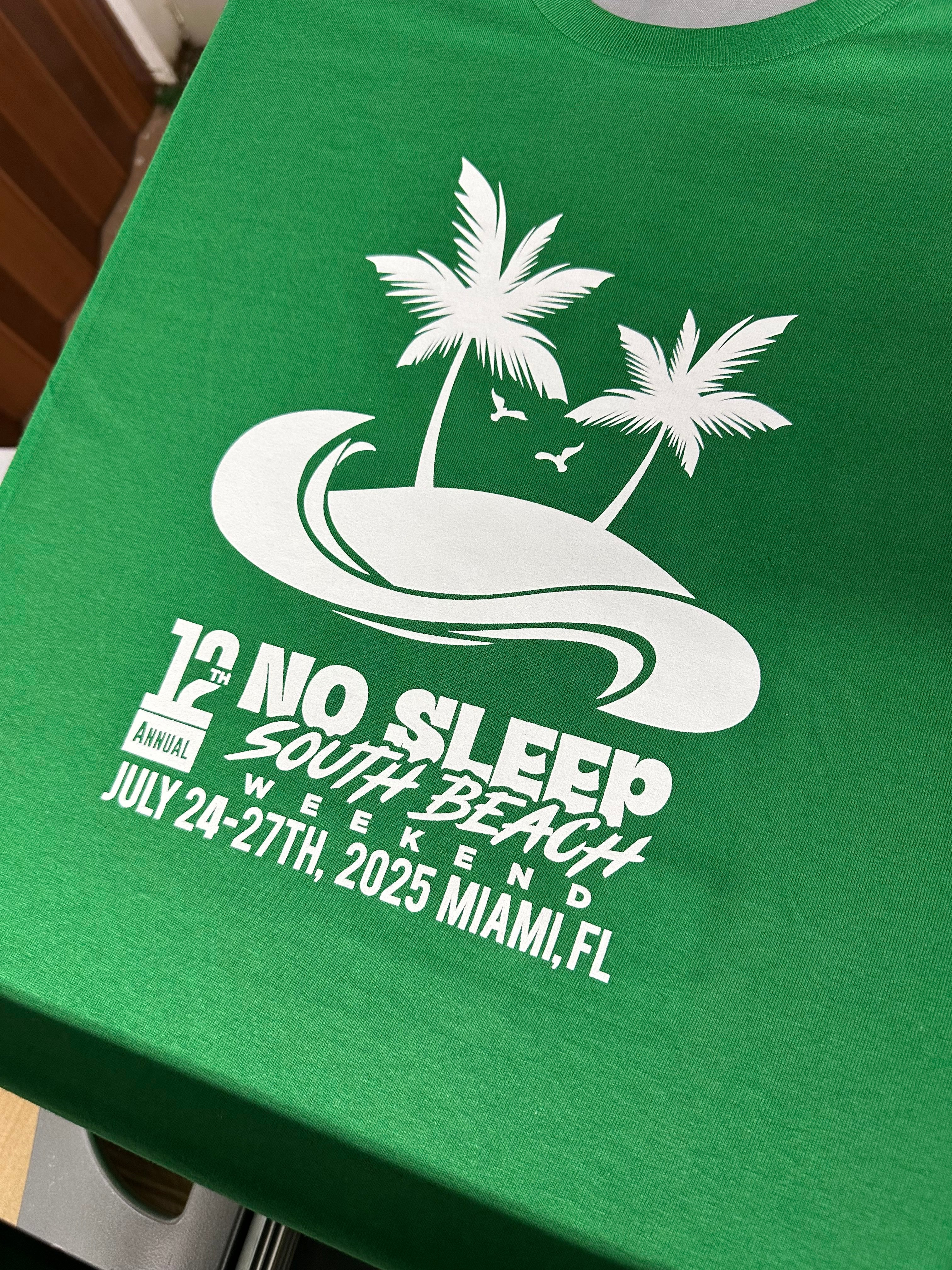 Green t-shirt with white graphic design featuring palm trees and text on a wooden surface.