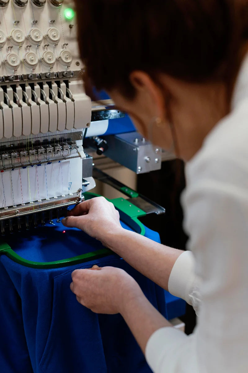 Person operating an embroidery machine with a close-up of the machine's needle area.