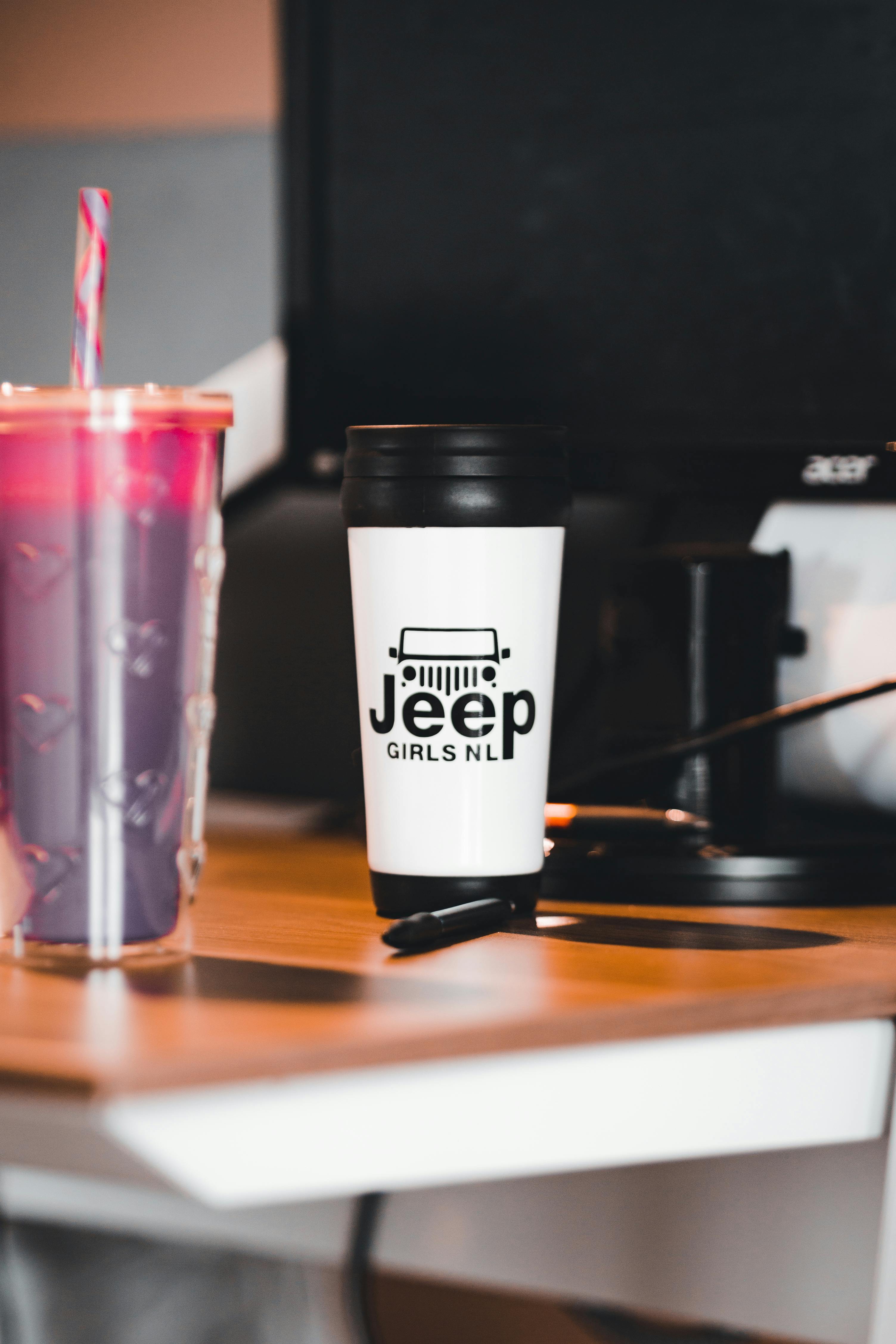 White custom printed travel mug with Jeep logo on a desk next to a purple drink.