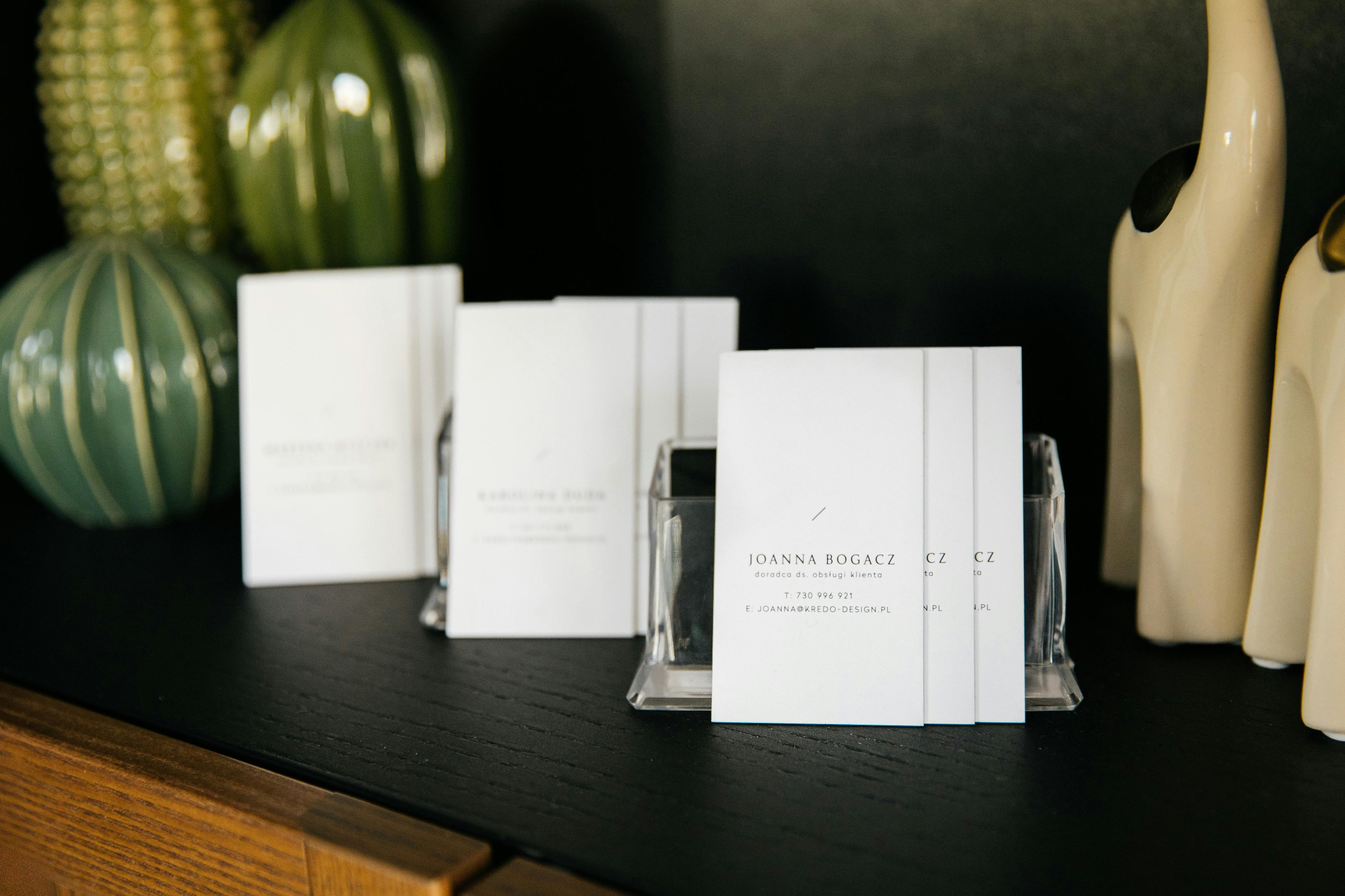 Stack of business cards with black text on a dark surface with decorative items.
