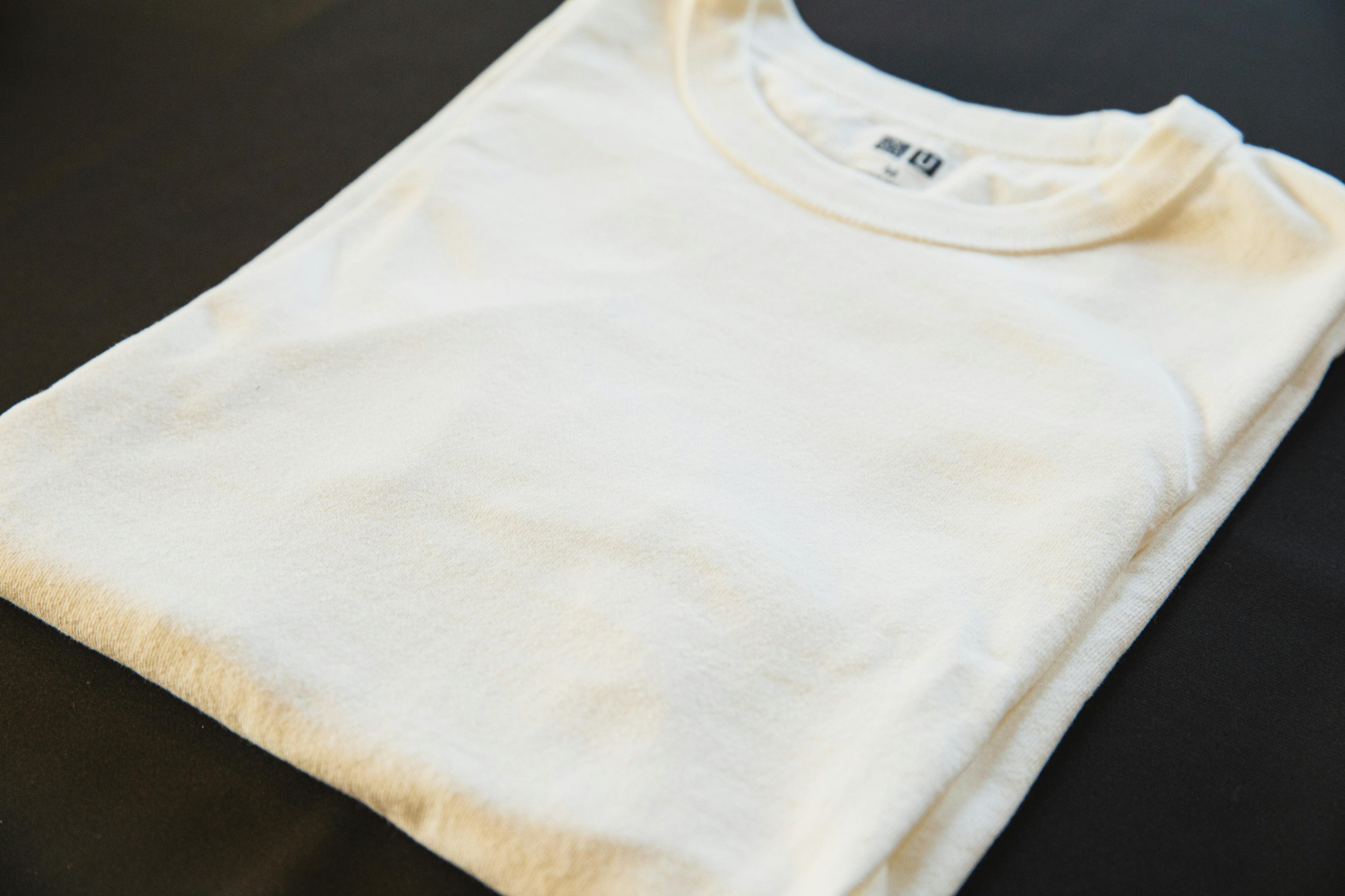 Folded white t-shirt with a brand logo on a dark surface