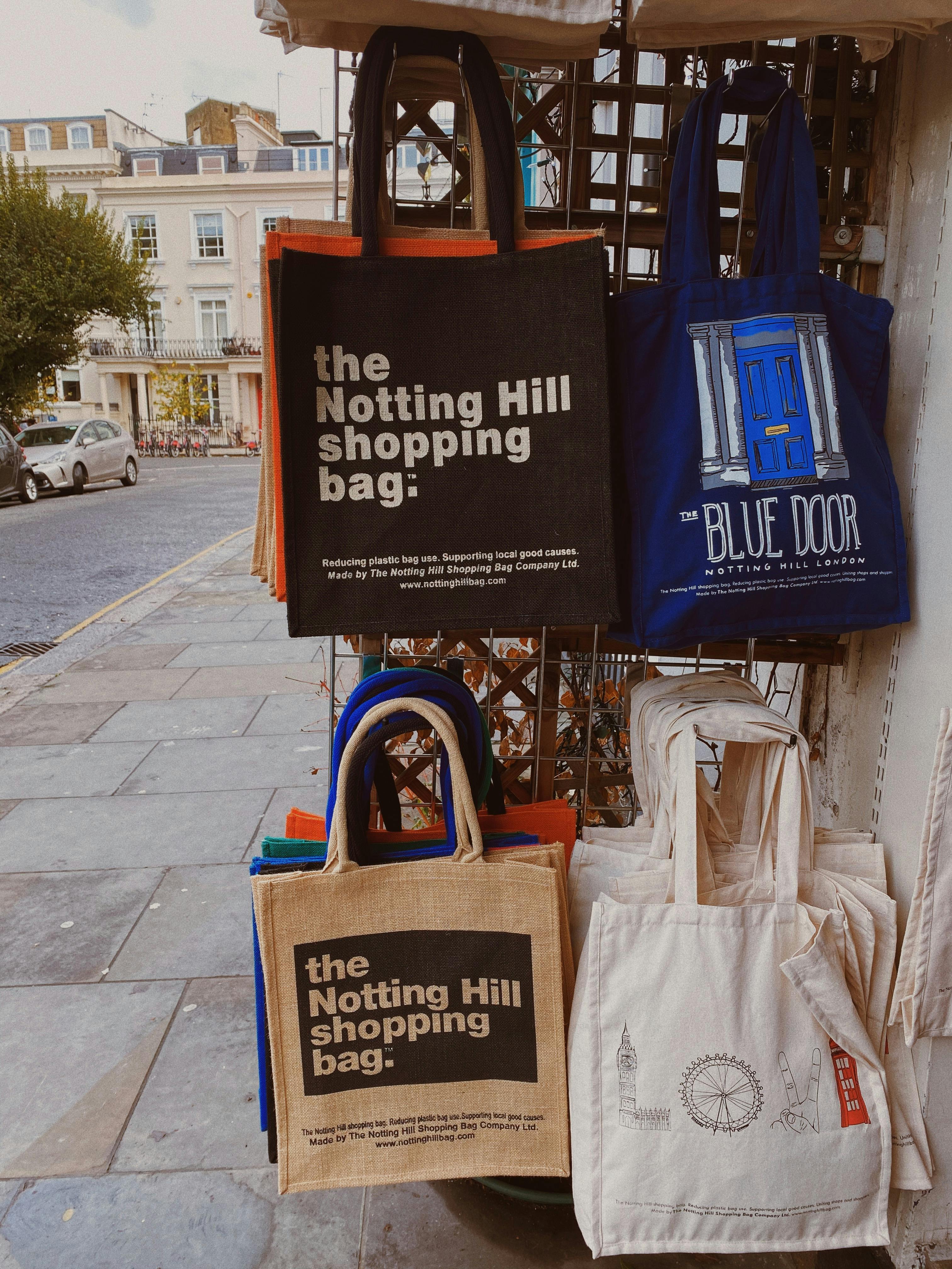 Collection of tote bags, including 'Notting Hill shopping bag' and 'Blue Door' design, displayed outdoors.
