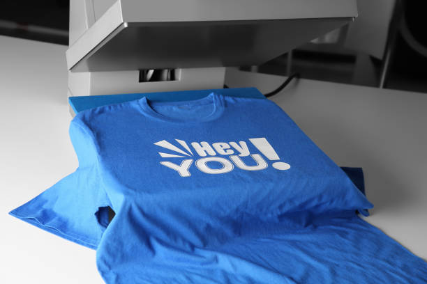 Blue t-shirt with 'Hey You!' text being printed on a machine.