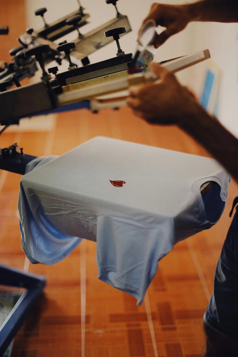 Person using a screen printing machine on a t-shirt with a red design.