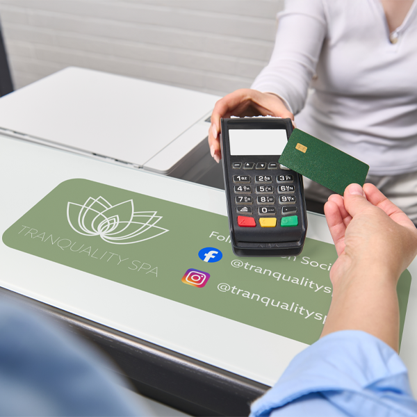 Person using a card reader with a Tranquality Spa branded mat in the foreground